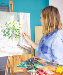 girl artist with a palette of paints draws paintings in an art studio. Palettes and easel,