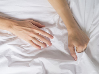 Hand clutches grasps a white crumpled bed sheet in a hotel room, a sign of ecstasy, feeling of...