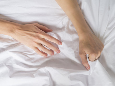 Hand clutches grasps a white crumpled bed sheet in a hotel room, a sign of ecstasy, feeling of pleasure or orgasm. Orgasm is the greatest point of sexual pleasure or a climax of sexual excitement