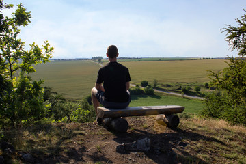 Young man sitting on bench on nature lookout, Czech landscape