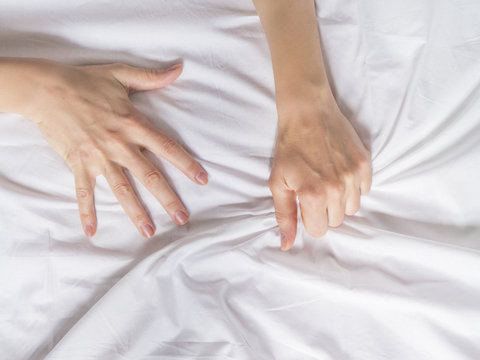 Hand clutches grasps a white crumpled bed sheet in a hotel room, a sign of ecstasy, feeling of pleasure or orgasm. Orgasm is the greatest point of sexual pleasure or a climax of sexual excitement