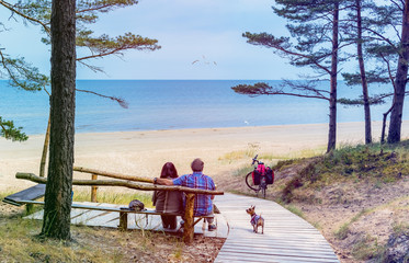 Happy couple of seniors are resting on wooden bench and  looking at the distance on sandy beach of the Baltic Sea. Image slightly toned. Concept of holiday at sandy beach
