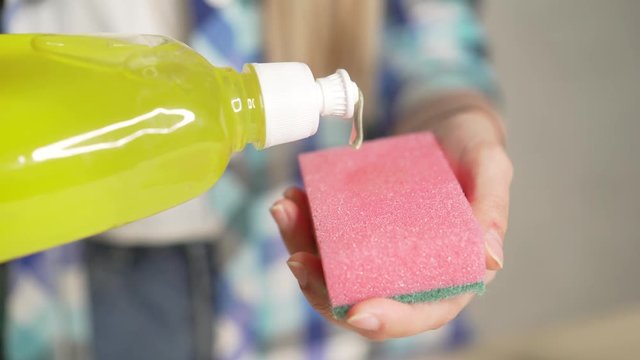 Means for washing dishes, chores casual plaid shirt fabrics people concept. Closeup of a lady cleaning the plates using a viscous detergent. Girl washing dishes. A drop of detergent on the sponge