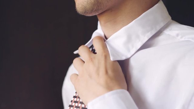 Handsome man in white shirt tying a tie. 3840x2160