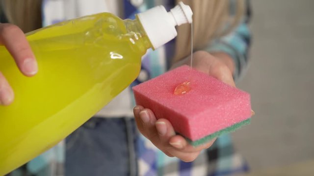 Means for washing dishes, chores casual plaid shirt fabrics people concept. Closeup of a lady cleaning the plates using a viscous detergent. Girl washing dishes. A drop of detergent on the sponge