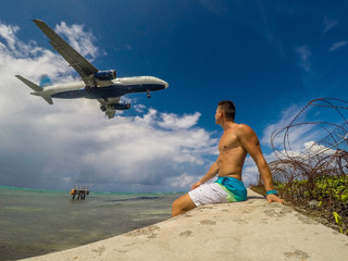 Muscular man on the coast watching landing of airplane flying over the sea of caribbean sea. Montego Bay. Jamaica. 2017