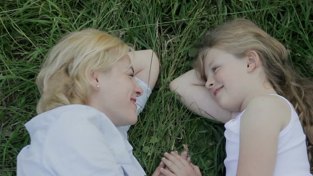 Mother and daughter lying on grass, smiling and putting their hands together.