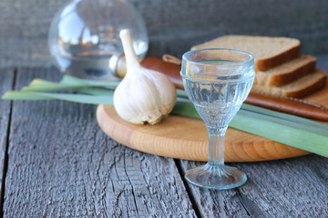 A glass of vodka, garlic, onion and bread on a wooden background.