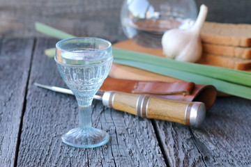 A glass of vodka, garlic, onion and bread on a wooden background.