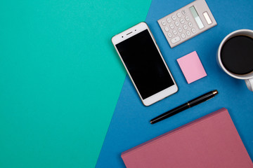 Office table desk with smartphone and other office supplies on green and blue background. Top view with copy space, flat lay.