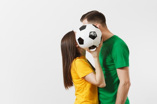 European young couple, woman man in love, football fans in yellow green t-shirt cheer up support team kissing behind soccer ball isolated on white background. Sport, family leisure, lifestyle concept.