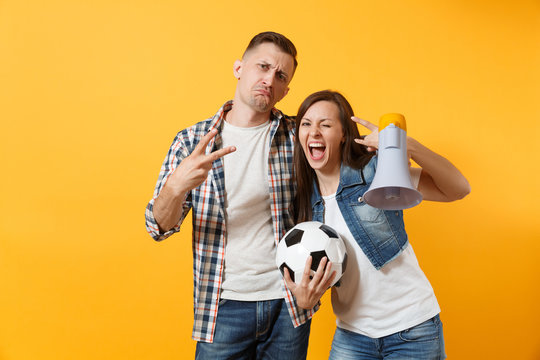 Young happy cheerful couple supporter, woman man, football fans cheer up support team, holding megaphone, soccer ball isolated on yellow background. Sport, family leisure, people lifestyle concept.