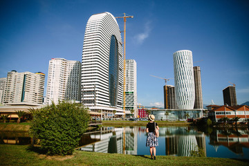 Tourist girl in a hat and with a backpack on the background of modern high-rise buildings in...