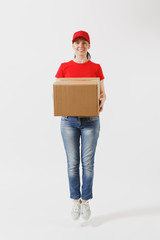 Full length portrait of fun delivery woman in red cap, t-shirt isolated on white background. Female courier or dealer jumping with empty cardboard box. Receiving package. Copy space for advertisement.