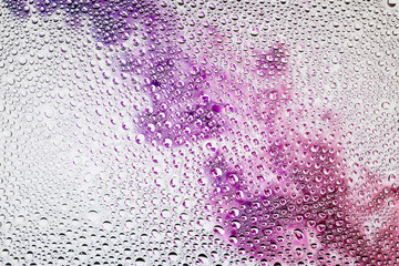 Close-up of a drop of water against a  purple, pink and red smoke on white backdrop, condensation on a gradient background