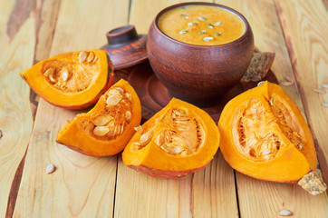 Pot pumpkin soup with sliced yellow pumpkins and seeds on the wooden background. Traditional autumn food or thanksgiving dish. SIde view