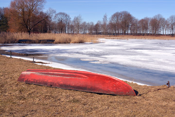 Red old boat on  early lake coast and ice