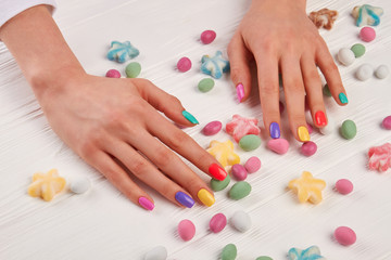 Obraz na płótnie Canvas Female hands with summer manicure. Young woman gentle hands with pastel manicure and colorful candies, white wooden background.