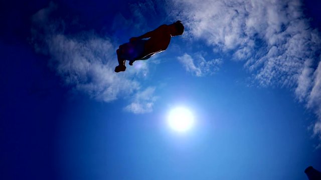 Young guy dark silhouette jumping on the trampoline on sky sun background slow motion sport activity