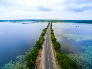Fototapeta premium Landscape of an asphalt road. View from above on the road going along the blue river. Summer photography with bird's eye view