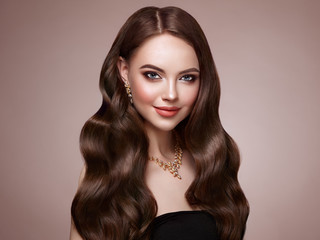 Brunette Girl with Long Healthy and Shiny Curly Hair. Care and Beauty. Beautiful Model Woman with Wavy Hairstyle. Make-Up and Jewelry