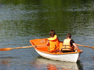 Couple in a life jackets floats on a rowing boat on a summer lake. Young man and woman in a boat,...