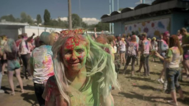 Young happy girl in colourful powder is jumping and shaking head on holi festival in daytime in summer, color concept