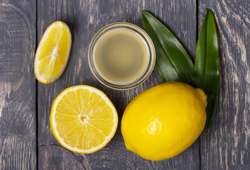 Lemon and fruit pieces, juice in bowl on wooden surface