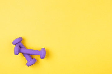Two violet dumbbells on yellow background. Top view, copy space.