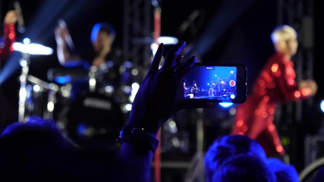 Fan spectator stay by concert stage hold mobile phone shooting video of music performance in night lights lumiere
