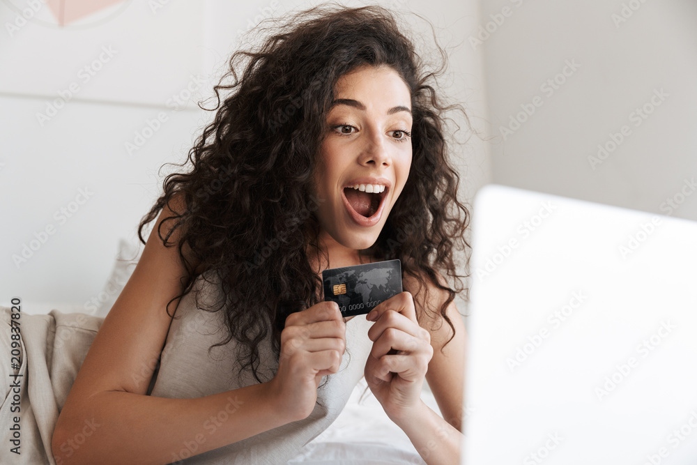 Poster caucasian woman with long curly hair wearing silk leisure clothing lying in bed with white linen in 