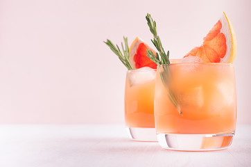 Two elegance cold wet drinking glasses with fresh grapefruit summer cocktail, ice, rosemary on pink...