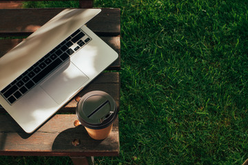 close up view of disposable cup of coffee and laptop on wooden bench