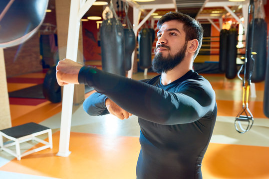 Bearded confident man in sportswear training box technique with punching bag in contemporary gym. 