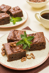 Brownie sweet chocolate dessert with walnuts and meant leaves on craft plate and cup of black coffee.
