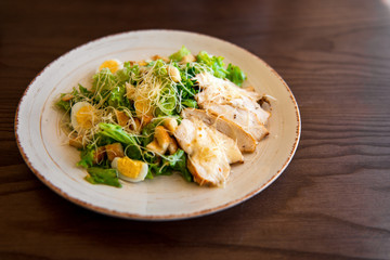 Fresh summer salad Ceasar with eggs, lettuce, chicken and parmesan cheese on white plate on wooden background; healthy concept; side view