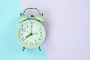 Vintage alarm clock on sweet pastel colored paper top view, background texture, pink, purple, yellow, beige, green and blue colour.