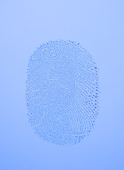 A fingerprint on glass from a thumb with a white / blue background.