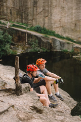 miling male travelers in protective helmets eating  food on rocky cliff over river