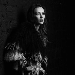 Full body portrait of gorgeous brunette woman wearing fashionable faux fur coat with long black and white hair and over knee boots. Seductive female model posing against gray brick wall on background.