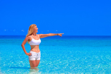 Gorgeous blond woman with white clothes is standing in the water at the sandy beach