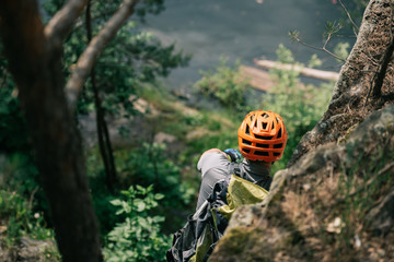 rear view of male hiker in protective helmet standing on rocky cliff in forest
