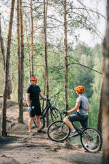 Fototapeta na wymiar Two male extreme cyclists in helmets with mountain bikes resting with sport bottles of water in forest