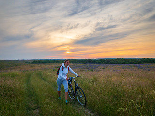 Woman with bicycle at meadow on sunset