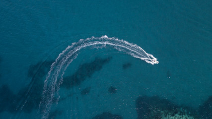 Aerial view of a white motorboat running on the azure waters of the Tyrrhenian Sea. On his trip near the coast the boat leaves a white trail in the waves ofeaves a white trail in the waves of the sea. - obrazy, fototapety, plakaty