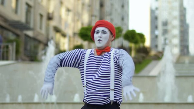 Funny mime in red beret gesticulate hands at fountains background