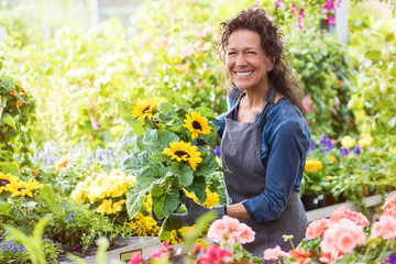 Freudig lachende Floristin im Gewächshaus mit einem Topf Sonnenblumen