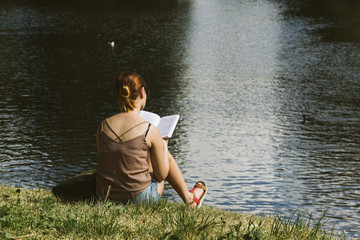 girl reading a book sitting near the pond