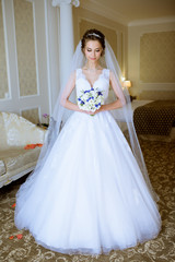 Fototapeta premium Beauty bride in bridal gown with bouquet and lace veil indoors