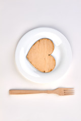 White plate with plywood heart. Plywood heart and on plate and wooden fork isolated on white background.